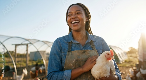 Happy female farmer holding a white chicken while smiling warmly on an organic poultry farm during a sunny day in the countryside
