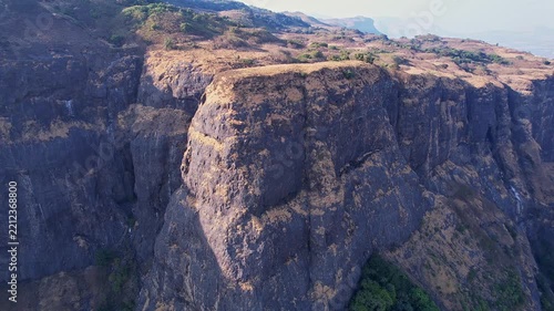 A drone video of majestic view of a rugged sunlit cliff side towering over deep mountain valleys