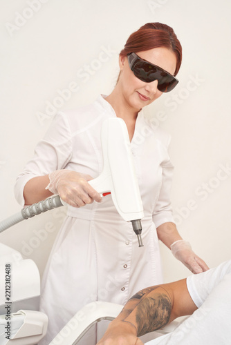 Female technician performing laser tattoo removal on patient s arm with advanced equipment in clinic.