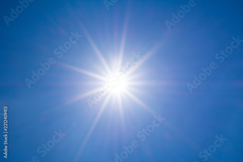 Bright sun shines in a clear blue sky with lens flare light ray beam background on a hot summer afternoon daylight