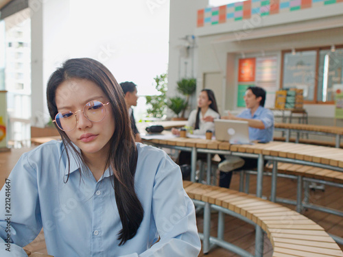 Thoughtful Asian Businesswoman Sitting Separately From Colleagues in Modern Office