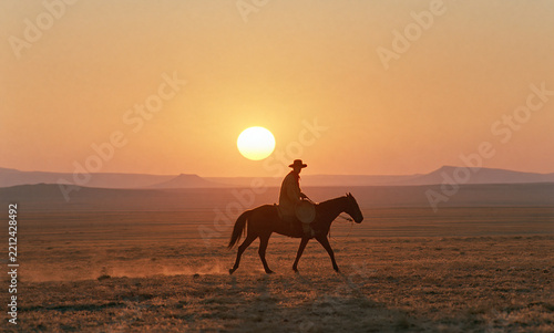  American Old West, an endless flat desert horizon with low mesas, a huge sun half sunk below the horizon line at sunset