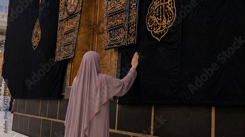 Muslim woman in hijab touching the Kaaba wall during Hajj pilgrimage