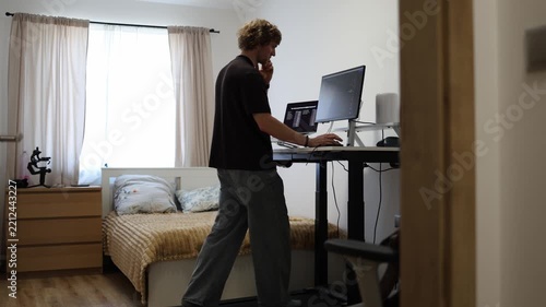 Young man works on a computer while walking on a treadmill combining office tasks with light exercise to stay physically active during long hours of screen based work at home
