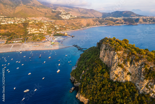 A breathtaking sunset aerial view captures Isola del Dino and the bay at Praia a Mare in Calabria, Italy. Boats navigate the deep blue waters along a sprawling beach, framed by dramatic coastal