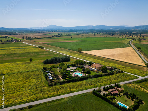 An aerial drone view reveals a charming Tuscan agriturismo nestled among vibrant sunflower fields and vast farmland. The property features a swimming pool and an organized camperstop for motorhomes in