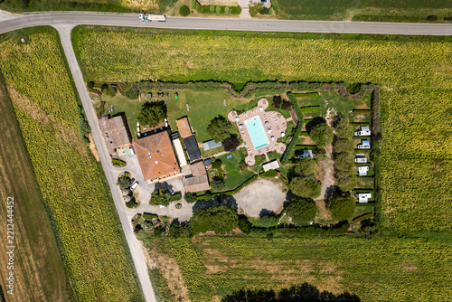 An aerial drone view reveals a charming Tuscan agriturismo nestled among vibrant sunflower fields and vast farmland. The property features a swimming pool and an organized camperstop for motorhomes in
