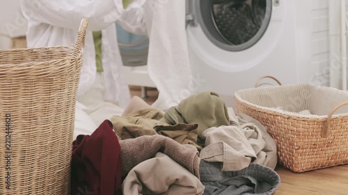 Young Asian woman sitting on the floor sorting a messy pile of clothes into laundry baskets.