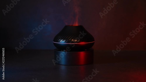Black ultrasonic humidifier rotating 360 degrees on a dark pedestal. Soft red and blue atmospheric lighting highlights its sleek rounded design in a minimalist studio setting.