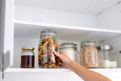 Hand taking a jar of colorful pasta from an organized kitchen pantry