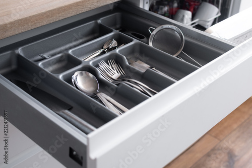 Close-up view of a neatly arranged cutlery drawer with spoons, forks, knives and kitchen utensils stored in a dark organizer tray in a modern home kitchen.