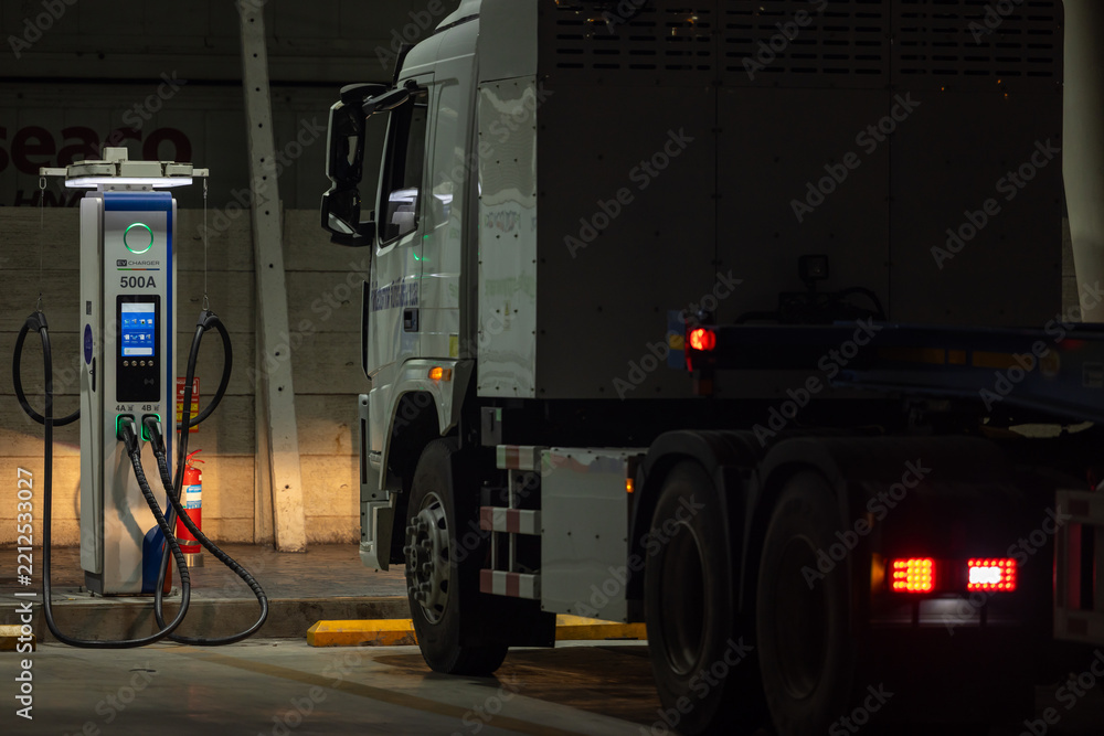 Fototapeta premium EV charging and semi truck electric vehicle, Electric vehicle semi truck trailer charging station for charge EV battery at night, EV charger semi truck trailer station at night.