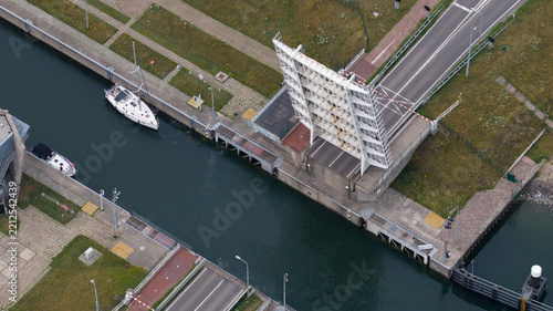 Aerial view of Zandkreeksluis bascule bridge with open span, boats waiting in the canal, and surrounding green landscape in Kortgene, Zeeland, Netherlands.