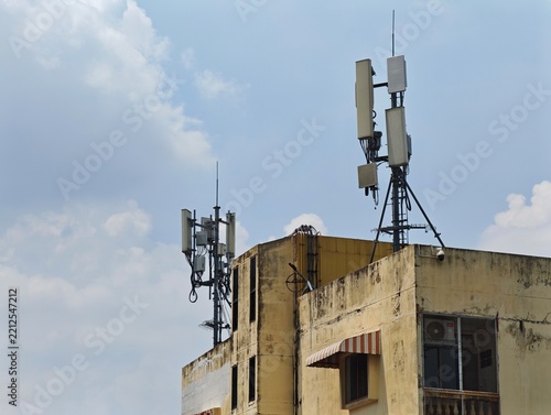 Fotografie Weathered building rooftop hosts two distinct telecommunications antenna arrays