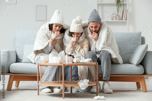 Ill family in warm hats coughing on sofa at home