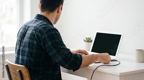 Man in plaid shirt connecting usb cable to laptop computer at white table 