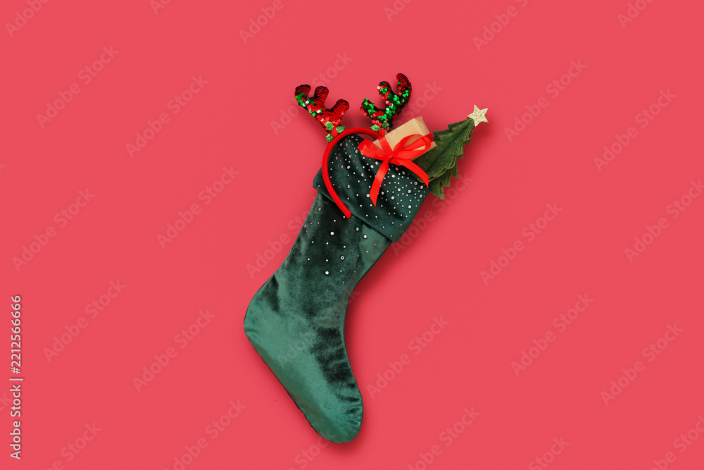 Obraz premium Christmas sock with reindeer horns, gift box and mini fir tree hanging on red wall