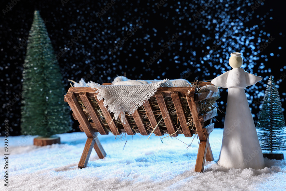 Obraz premium Manger with baby Jesus, angel and Christmas trees on snow against dark background