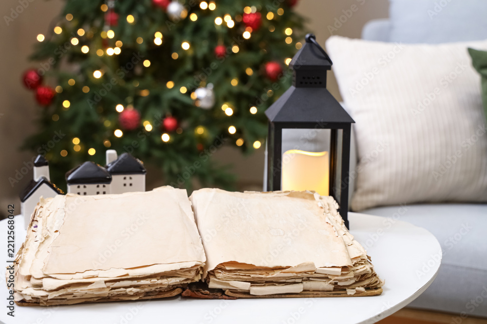 Obraz premium Opened old book and glowing lantern on table in living room, closeup. Christmas story concept