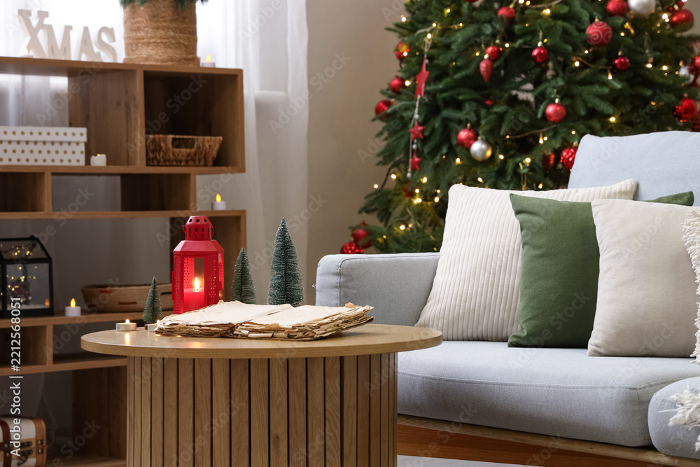 Obraz premium Opened old book, glowing lantern and candles on table in living room. Christmas story concept