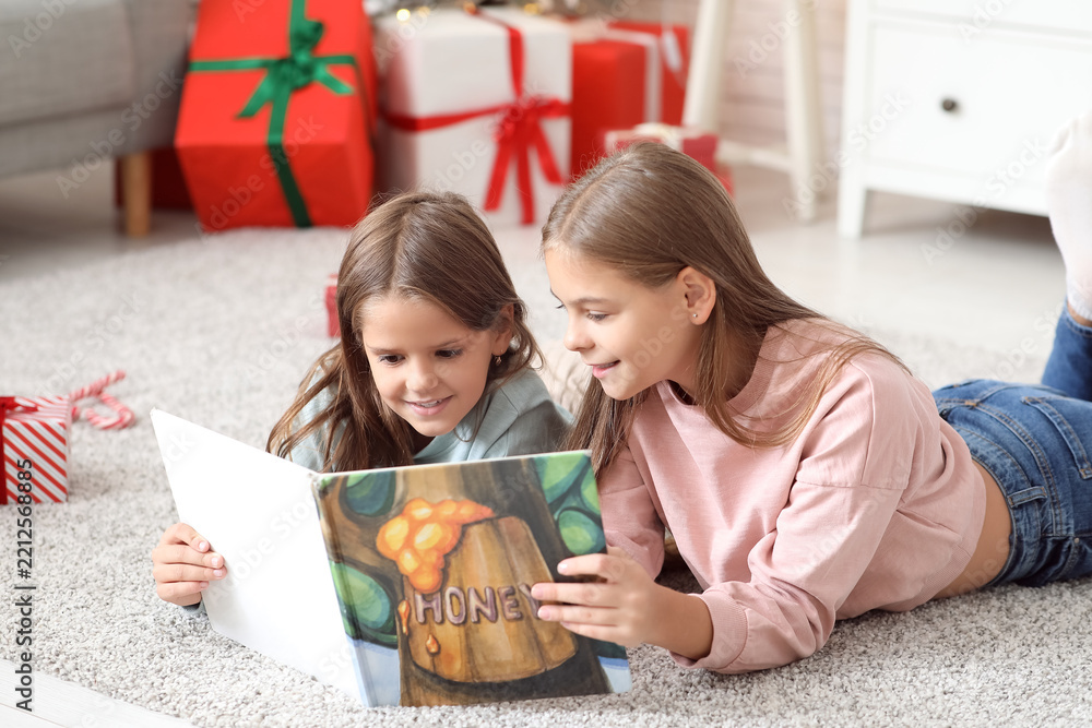 Obraz premium Cute happy little girls with book reading Christmas story at home