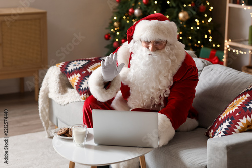Santa Claus with laptop video chatting on sofa at home