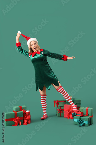 Happy young woman dressed as elf with Christmas gifts on green background