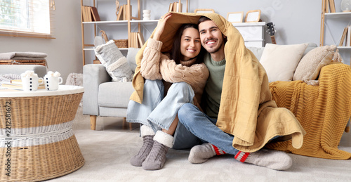 Loving couple with warm plaid sitting at home on winter day