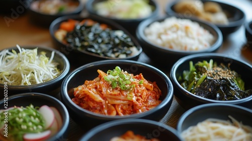 Assorted korean side dishes served in small black bowls arranged on a wooden table surface