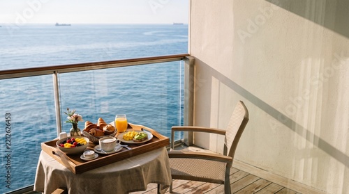Breakfast served on a private cruise cabin balcony overlooking calm blue water, refined cinematic travel imagery for hospitality and premium vacation promotions
