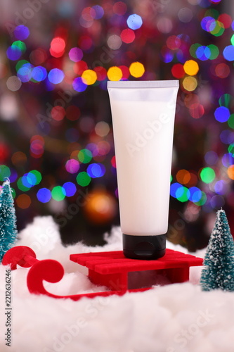 White cosmetic tube on red sled, winter skin treatment