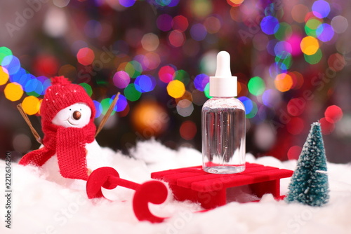 Bottle of serum on red sled, snow and Christmas lights background, winter skin care