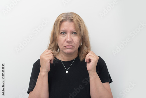 Middle-aged woman in black shirt with serious, concerned expression while holding her hair. Woman's hair starting to turn gray, she is very worried, aging concept, anti-aging