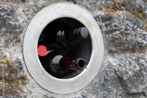 Brown glass wine bottles lie in special hole in the wall for recycling, people hand over bottles, cans, and glass here for further recycling and use