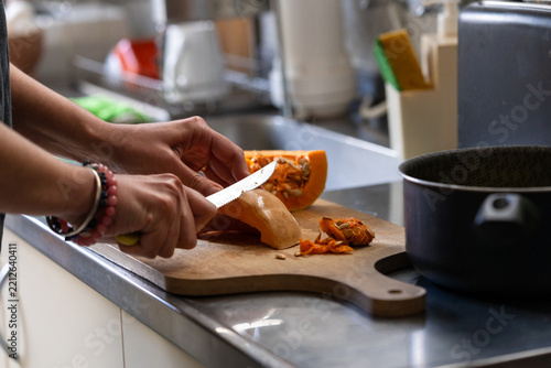 Person peeling and cutting pumpkin on a wooden board in the kitchen