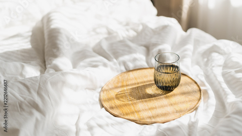 Glass of water on wooden tray on white bed linen