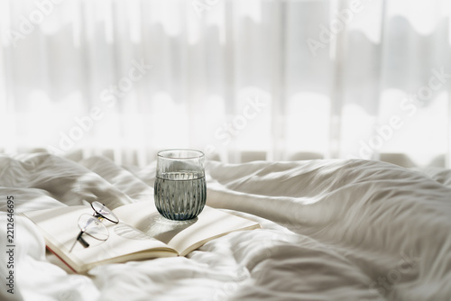 Open book and water glass on white bed linen