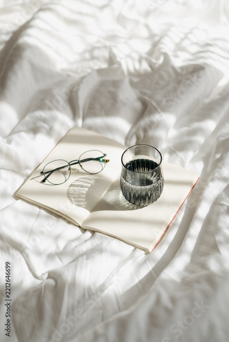 Open book with glasses and water glass on white bed linen