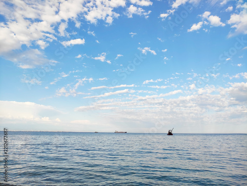 Panoramic view of calm sea surface with distant ships on the horizon under bright blue sky with fluffy white clouds, coastal landscape