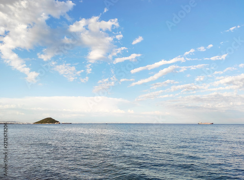 Panoramic view of calm sea surface with distant ships on the horizon under bright blue sky with fluffy white clouds, coastal landscape