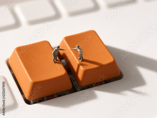 Miniature figures interacting on orange keyboard keys. Conceptual minimalism of office routine and digital communication. Macro photography of tiny people