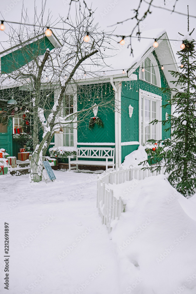 Obraz premium Vertical shot of snow covered wooden house decorated with Christmas lights and festive ornaments. Exterior winter scene suitable for holiday seasonal advertising and travel marketing