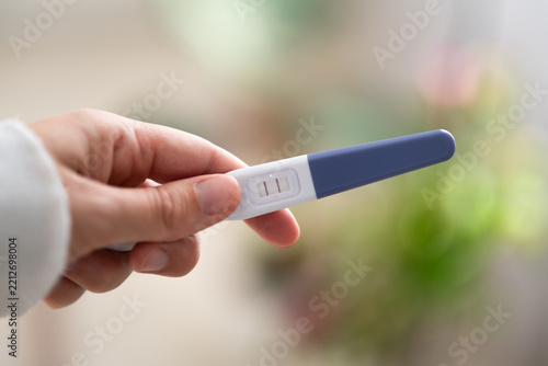 Obraz na plátně Close-up of hand holding home pregnancy test with two visible lines as positive result