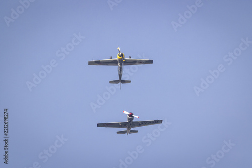View of two vintage propeller aircraft flying in formation against a clear blue sky over La Spezia, Liguria, Italy.