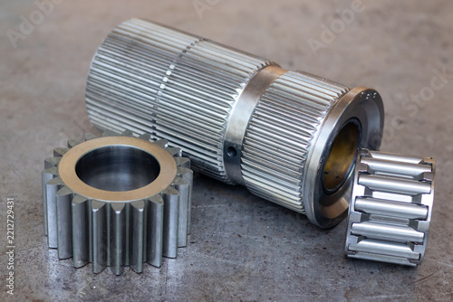 Metal transmission shaft rests with spur gear and needle roller bearing on workshop table.