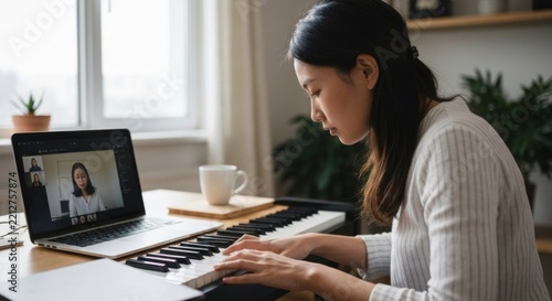 Asian woman taking a remote piano lesson, hands on keyboard, laptop showing teacher