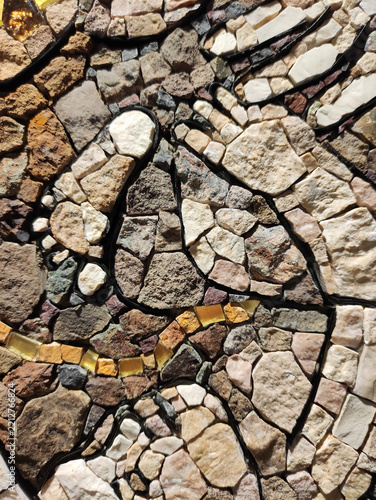 Detailed macro photograph of a multi-colored glass mosaic fragment, with small tiles arranged in flowing curved patterns. The surface is glossy and irregular, reflecting light