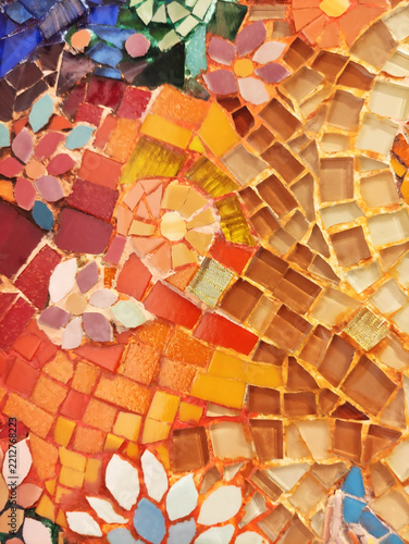 Detailed macro photograph of a multi-colored glass mosaic fragment, with small tiles arranged in flowing curved patterns. The surface is glossy and irregular, reflecting light