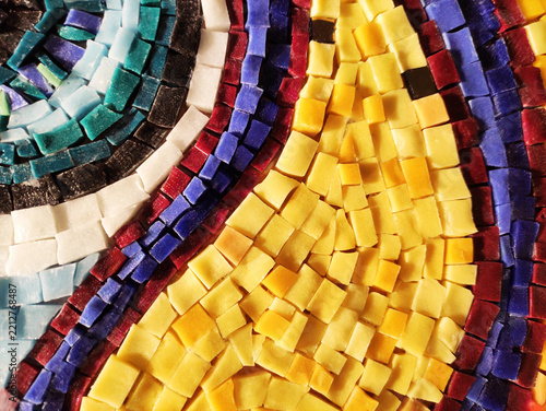 Detailed macro photograph of a multi-colored glass mosaic fragment, with small tiles arranged in flowing curved patterns. The surface is glossy and irregular, reflecting light