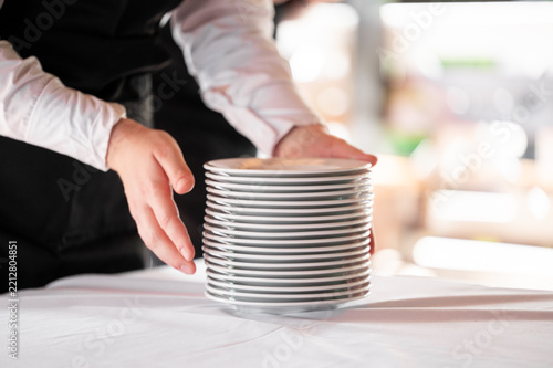 A stack of clean white ceramic plates on a table with a server's hands nearby, shallow depth of field.